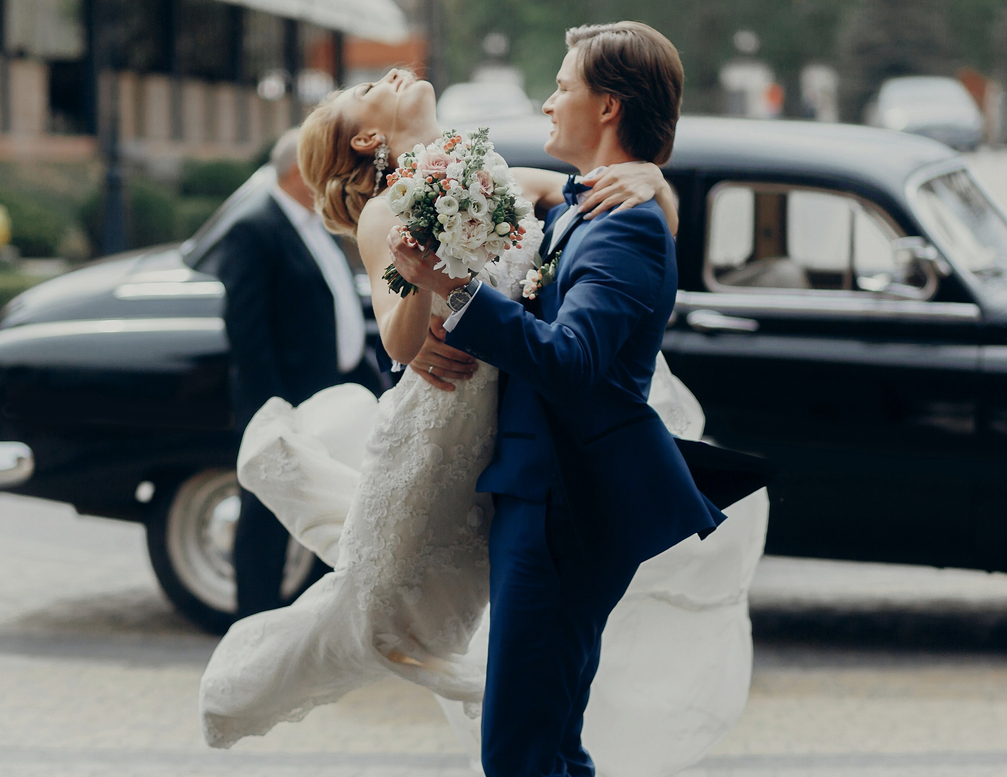 Nygift par som dansar med veteranbil i bakgrunden